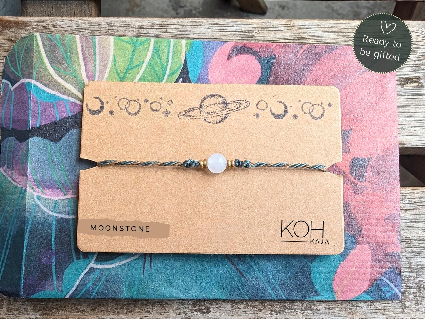 Makramee-Armband mit Mondstein präsentiert auf einer stilvollen, naturfarbenen Geschenkverpackung, verziert mit einem handgestempelten Planeten- und Mondmotiv. 'Ready to be gifted'